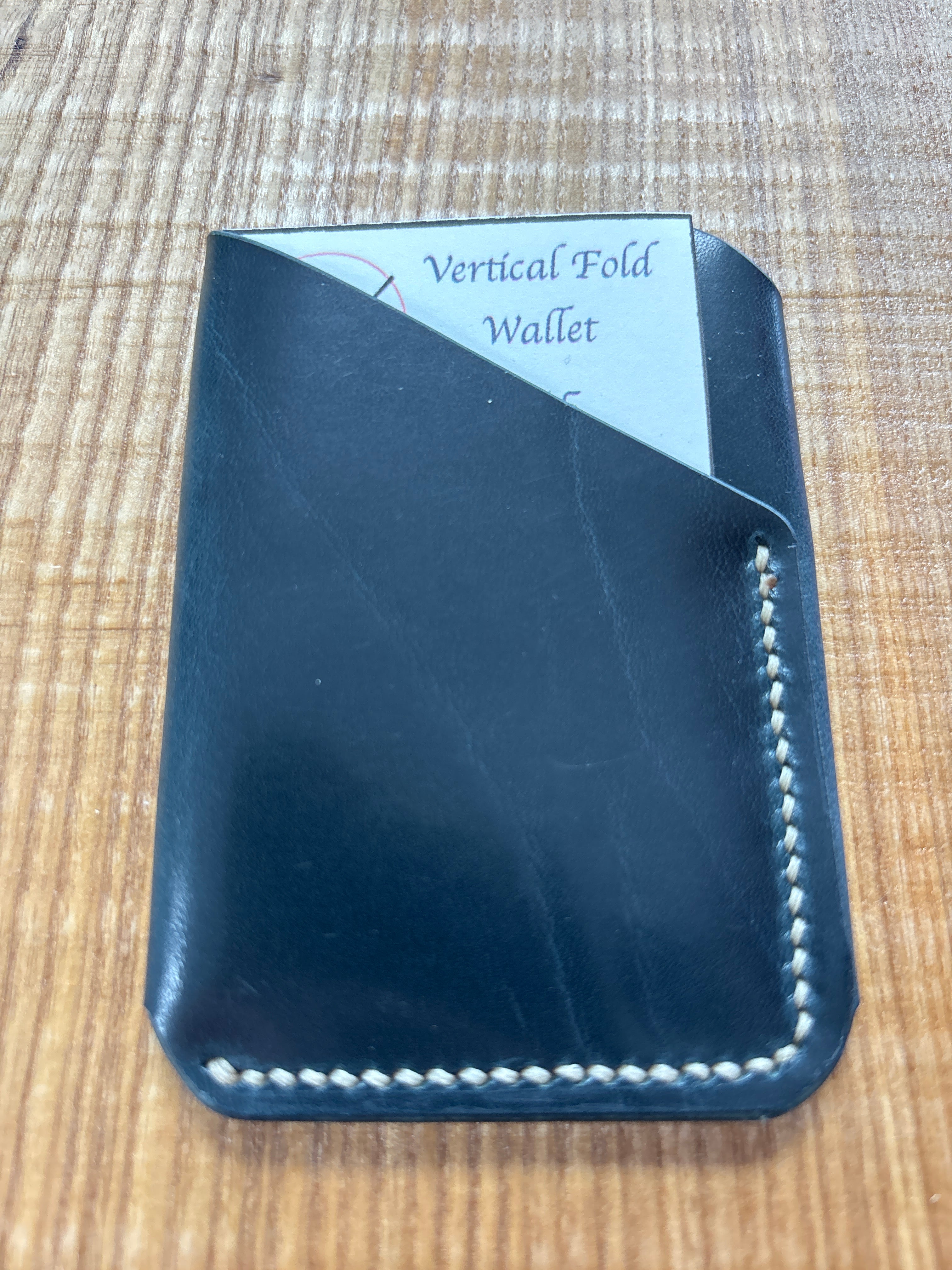 Black leather wallet with 'Vertical Fold Wallet' label on a wooden surface