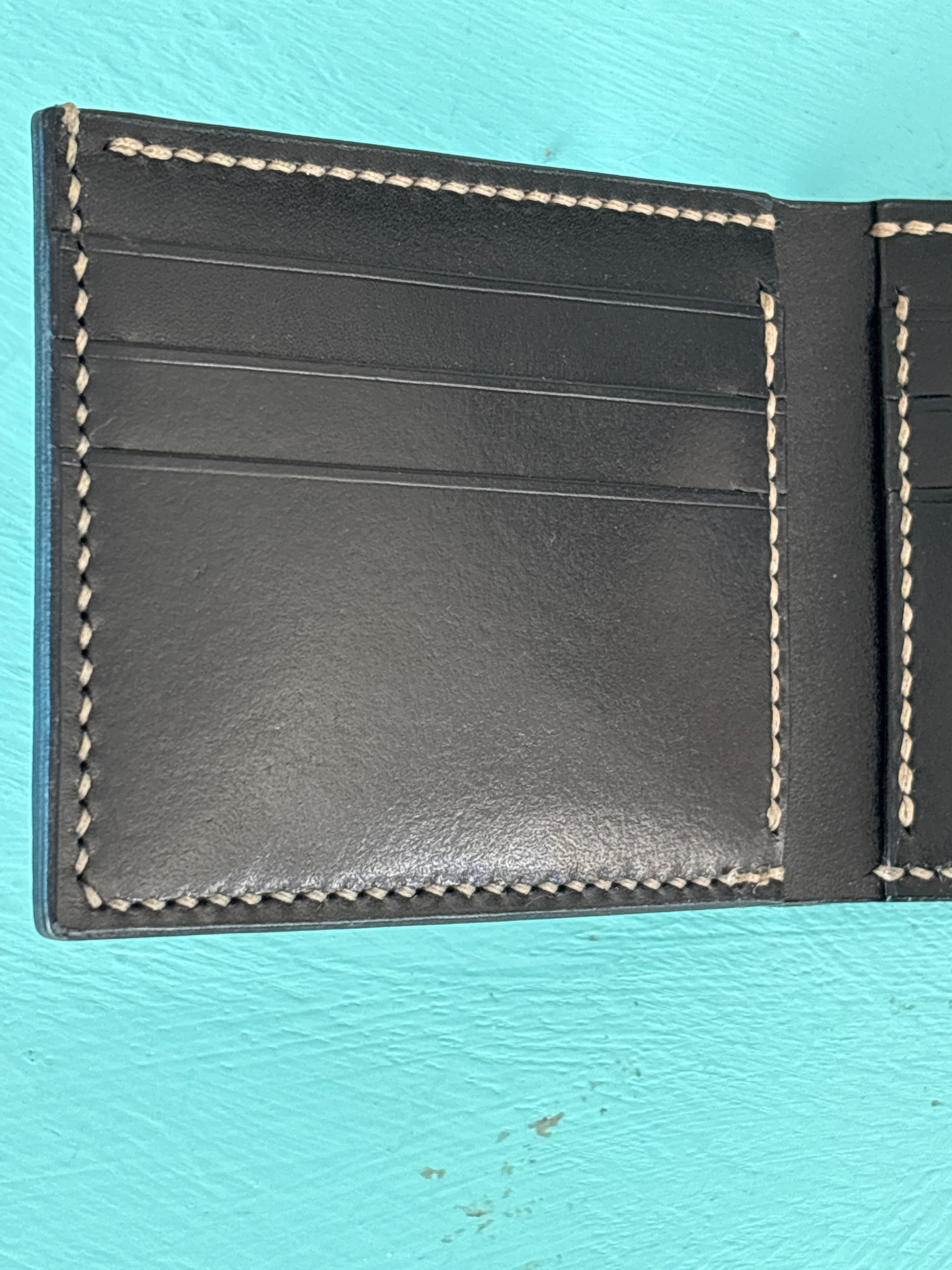 Black leather wallet with white stitching on a light blue background