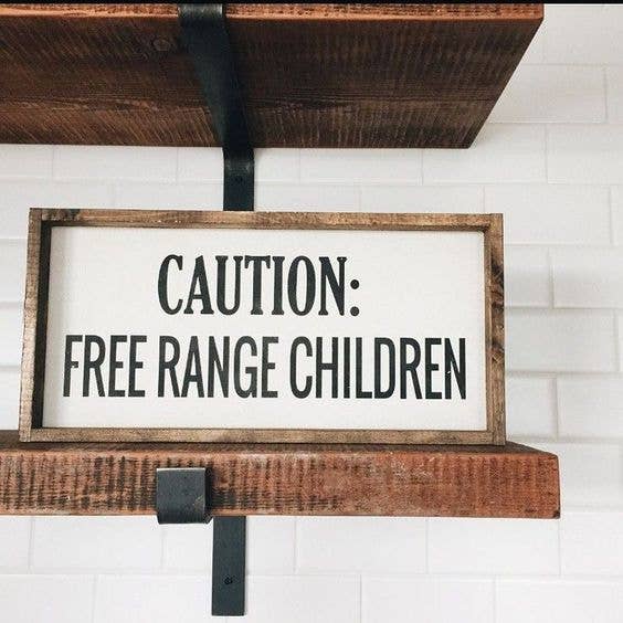 Wooden sign with 'CAUTION: FREE RANGE CHILDREN' text on a white tiled wall.