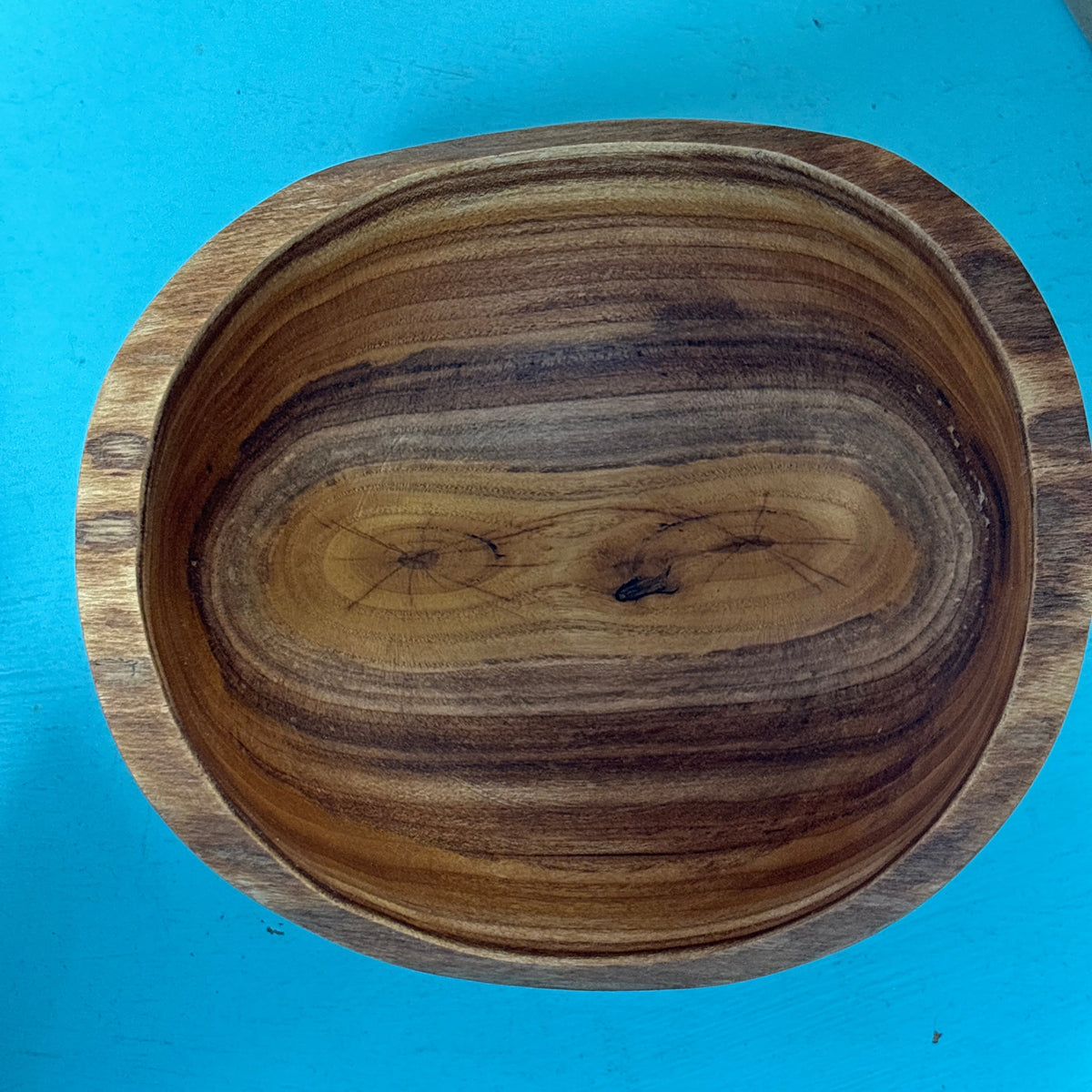 A round wooden bowl with a rich natural wood grain pattern, photographed from directly above on a bright blue background.