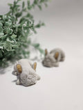 Two small CEMENT sculptures of animals on a light surface with greenery in the background