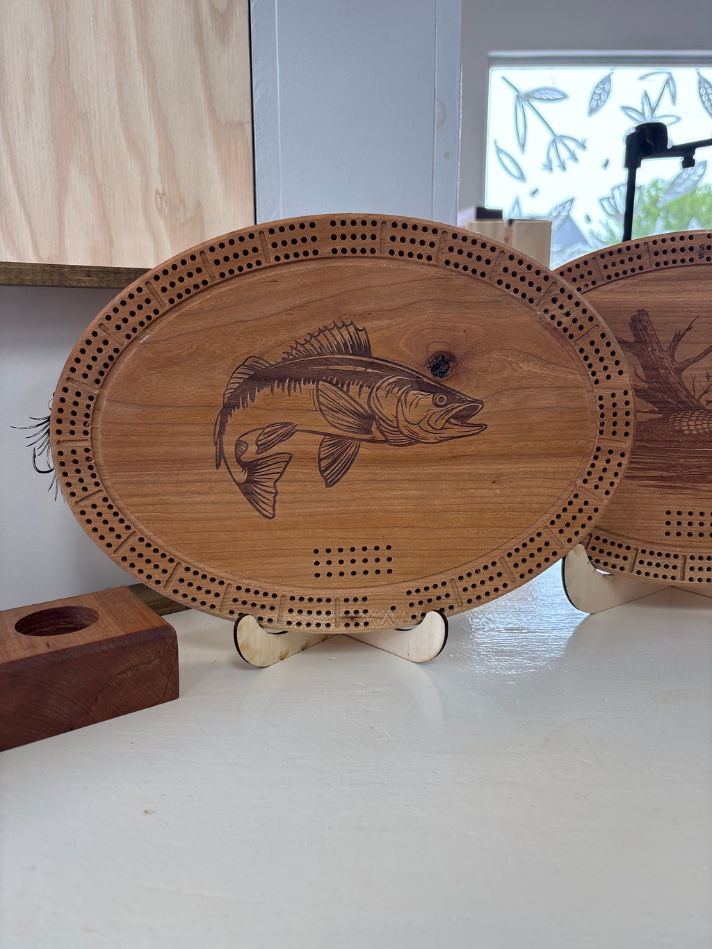 Wooden cribbage board with fish design on a stand indoors.