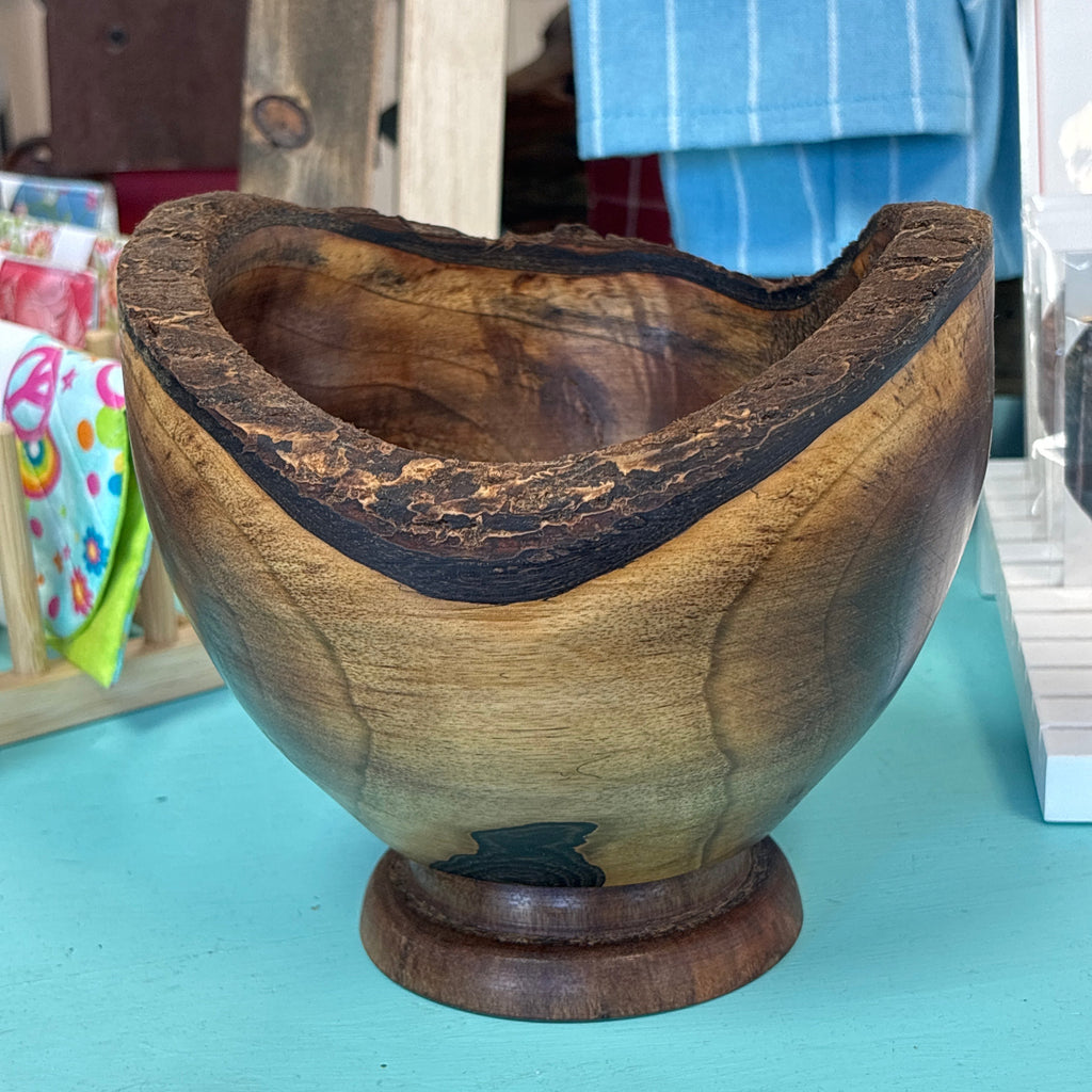 A rustic handcrafted wooden bowl with a live edge, displayed on a turquoise table in a shop setting.