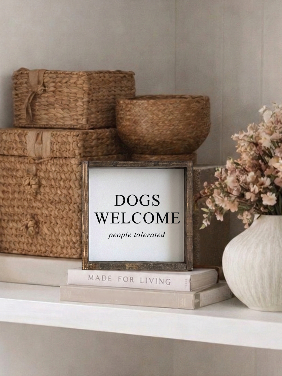 Decorative shelf with woven baskets, a framed sign, books, and a vase with flowers.