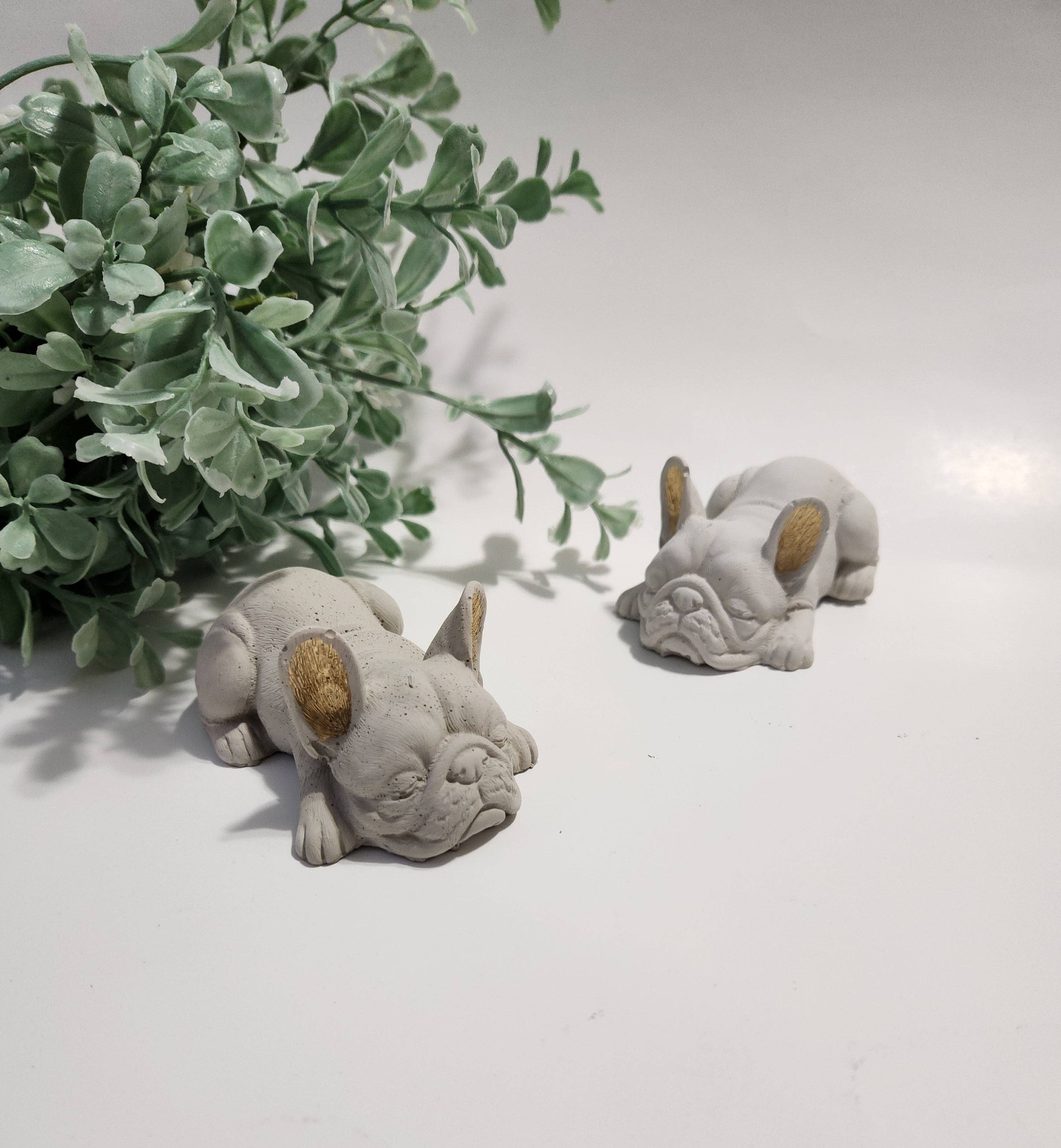 Two small stone sculptures of dogs on a light surface with a plant in the background