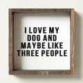 Wooden framed sign with text 'I love my dog and maybe like three people' on a white wall.