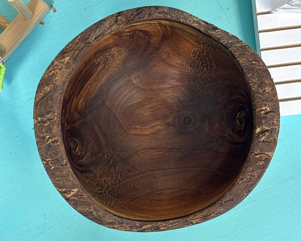 A round wooden bowl with a thick, textured dark brown rim, photographed from directly above on a bright turquoise surface.
