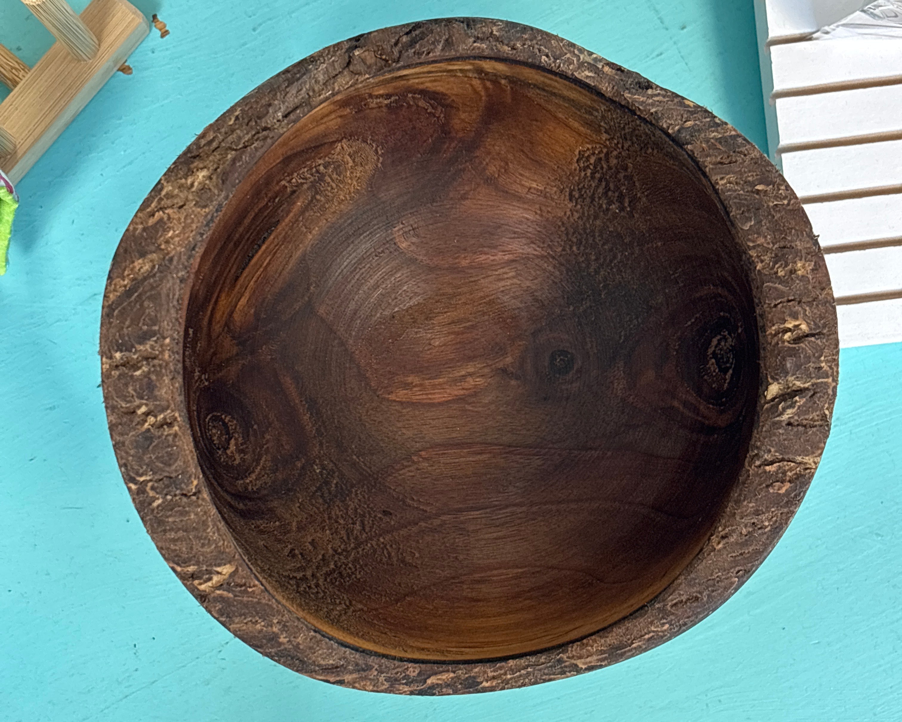 A round wooden bowl with a thick, textured dark brown rim, photographed from directly above on a bright turquoise surface.