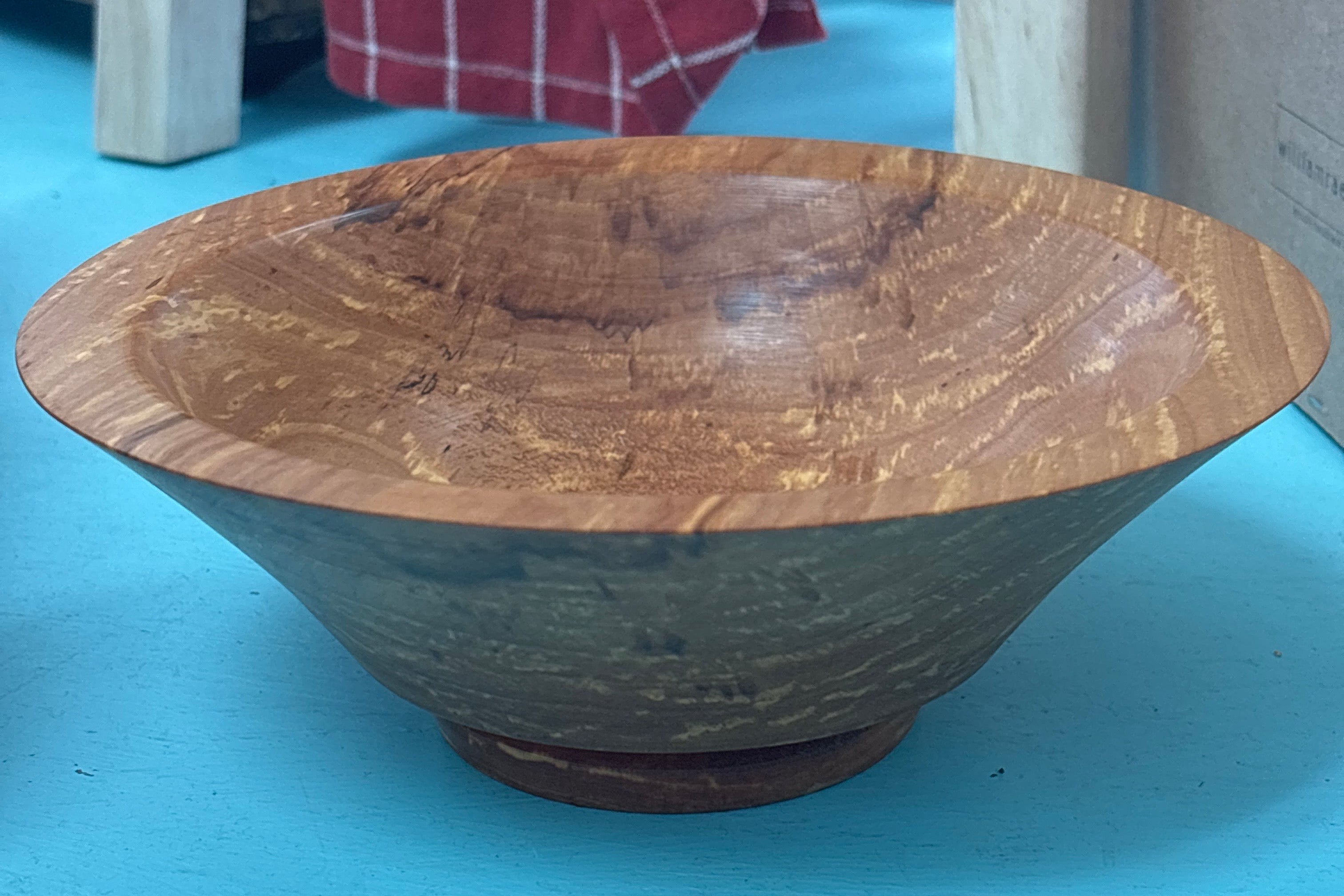A handcrafted wooden bowl with a rich, swirling grain pattern, resting on a bright turquoise surface.