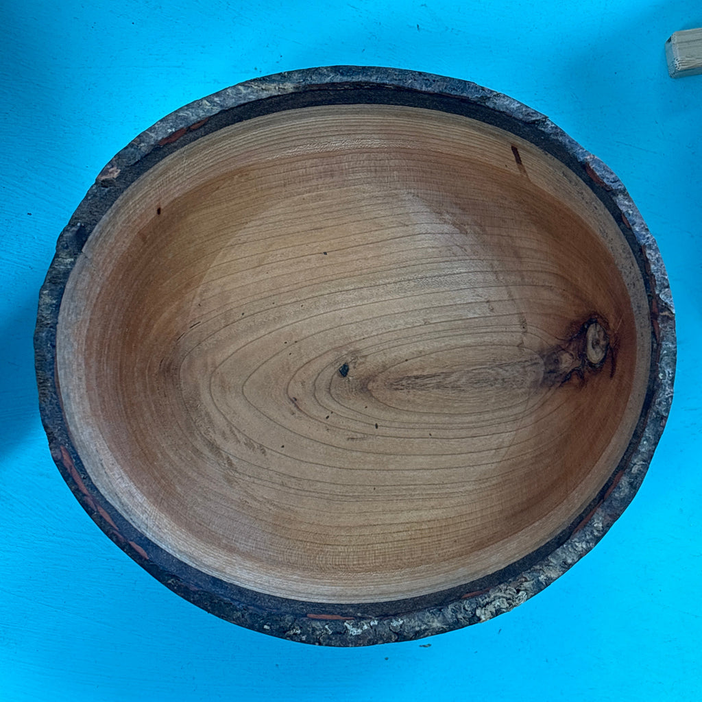 A rustic handcrafted wooden bowl with a natural bark edge, photographed from directly above on a bright blue background.