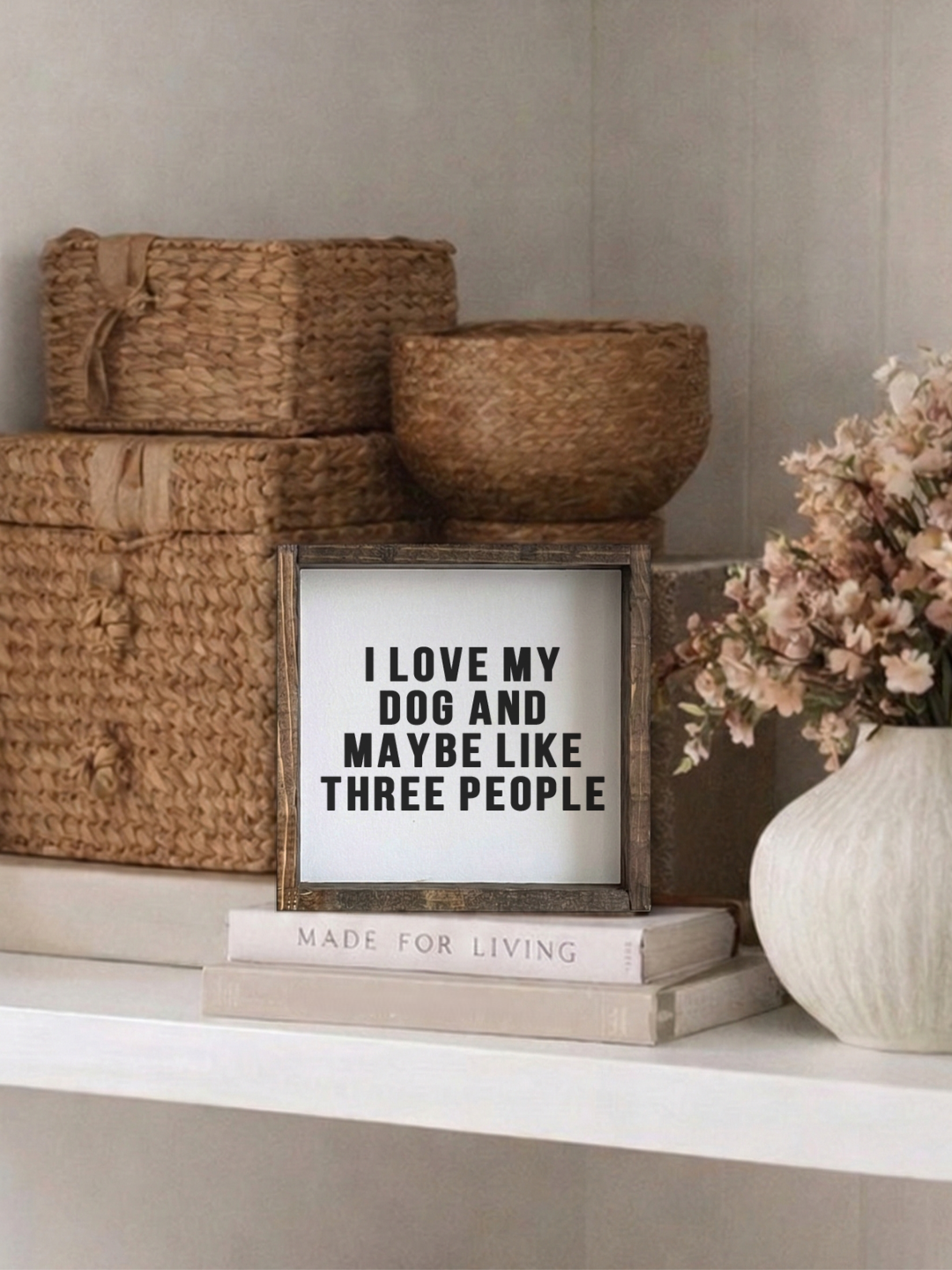 Decorative shelf with woven boxes, a framed quote, and a vase with flowers.
