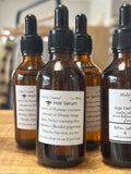 A brown bottle in a store setting on a wooden surface. A label on the bottle reads HAIR SERUM.
