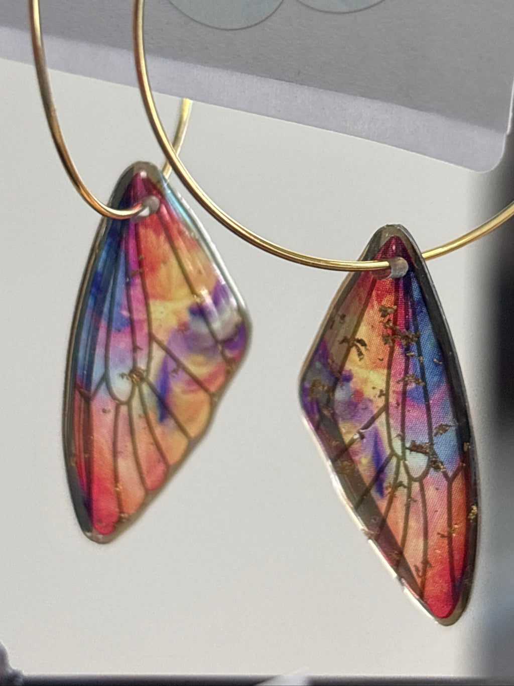 Butterfly wing earrings on a gold hoop with a price tag in the background.