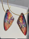 Butterfly wing earrings on a gold hoop with a price tag in the background.