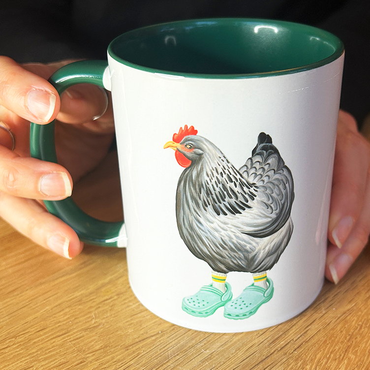Person holding a mug with a chicken design on a wooden table