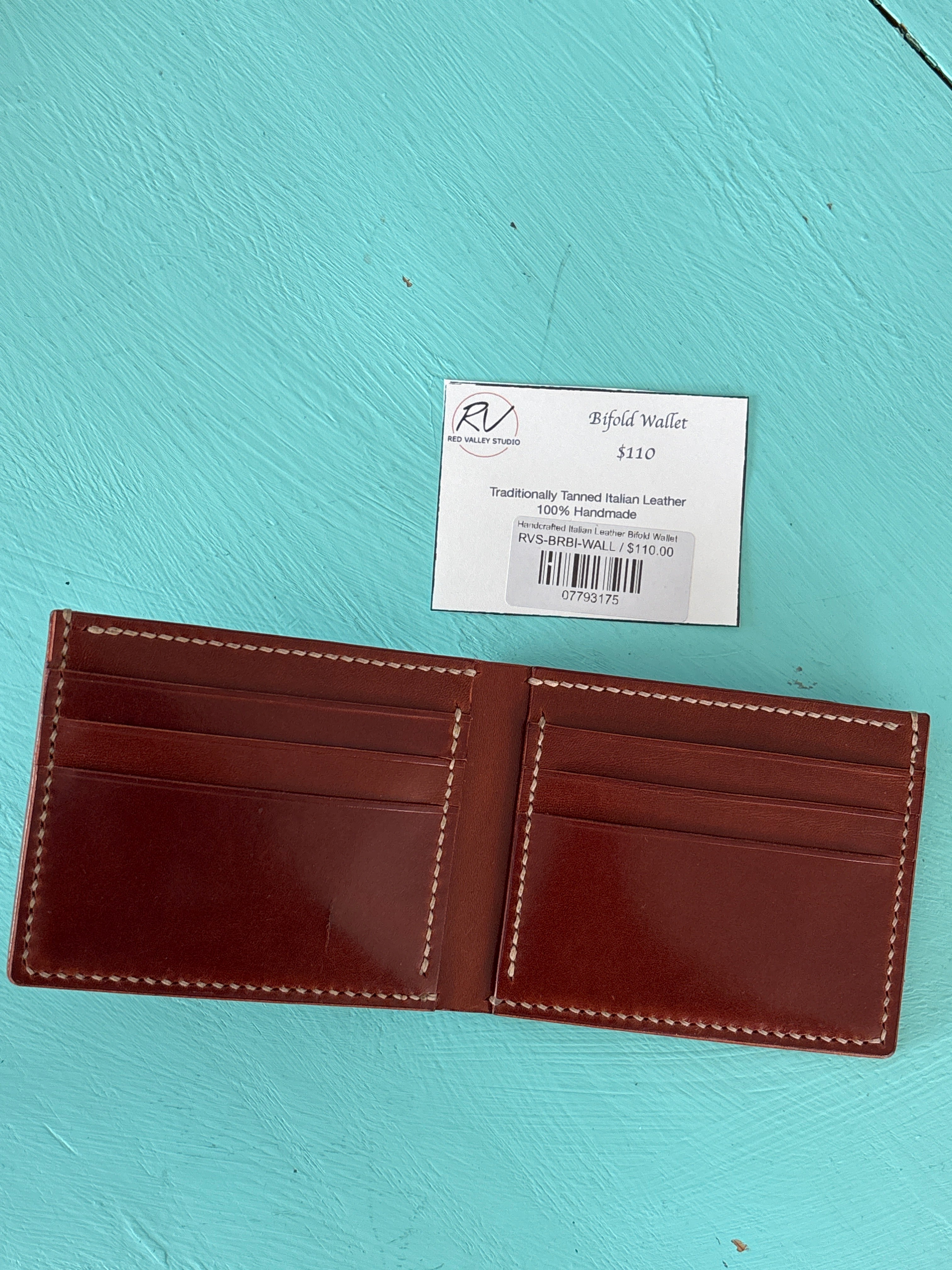 Brown leather wallet with visible stitching on a turquoise background, featuring a brand label.