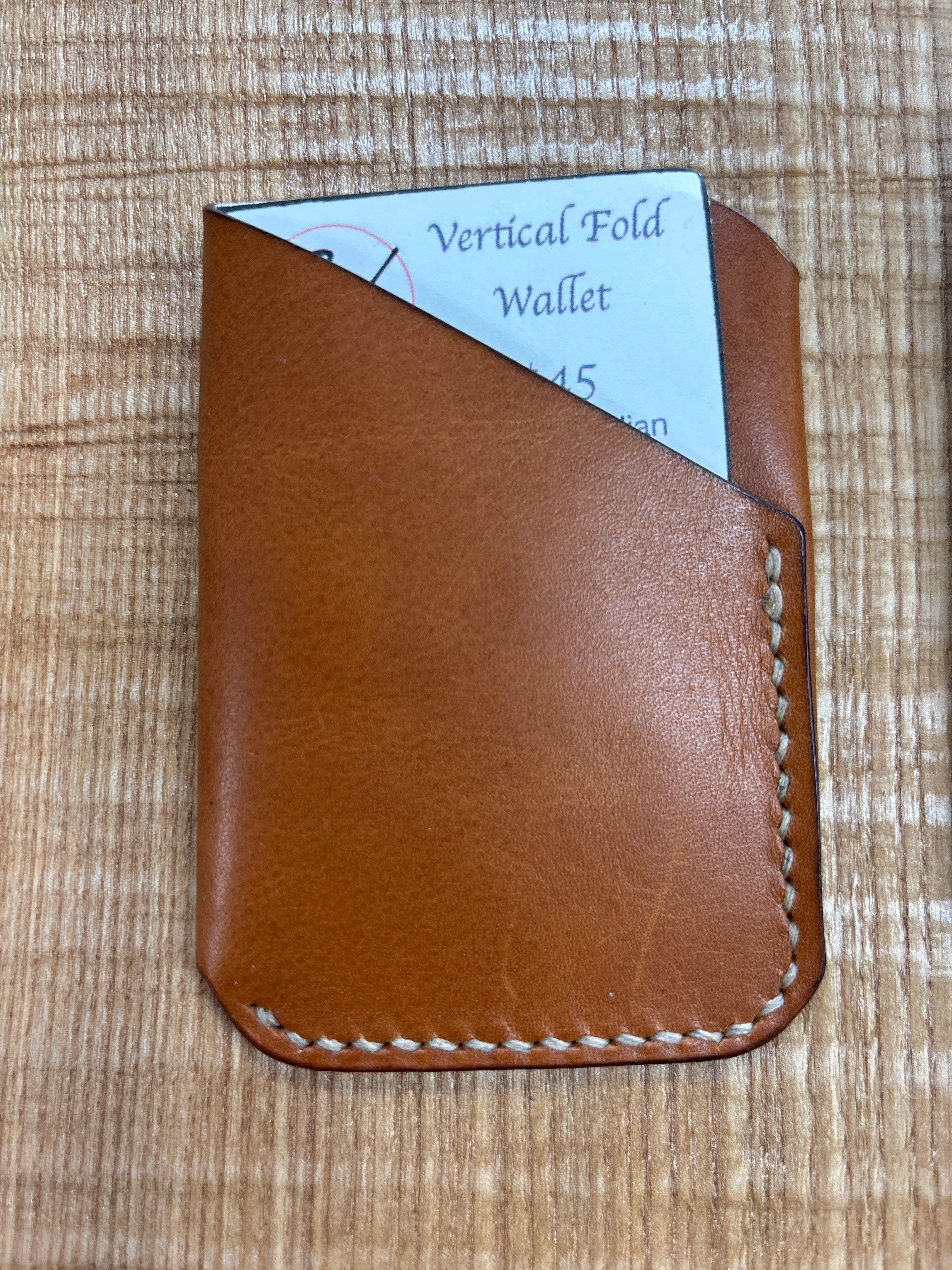 Brown leather wallet with white stitching on a wooden surface