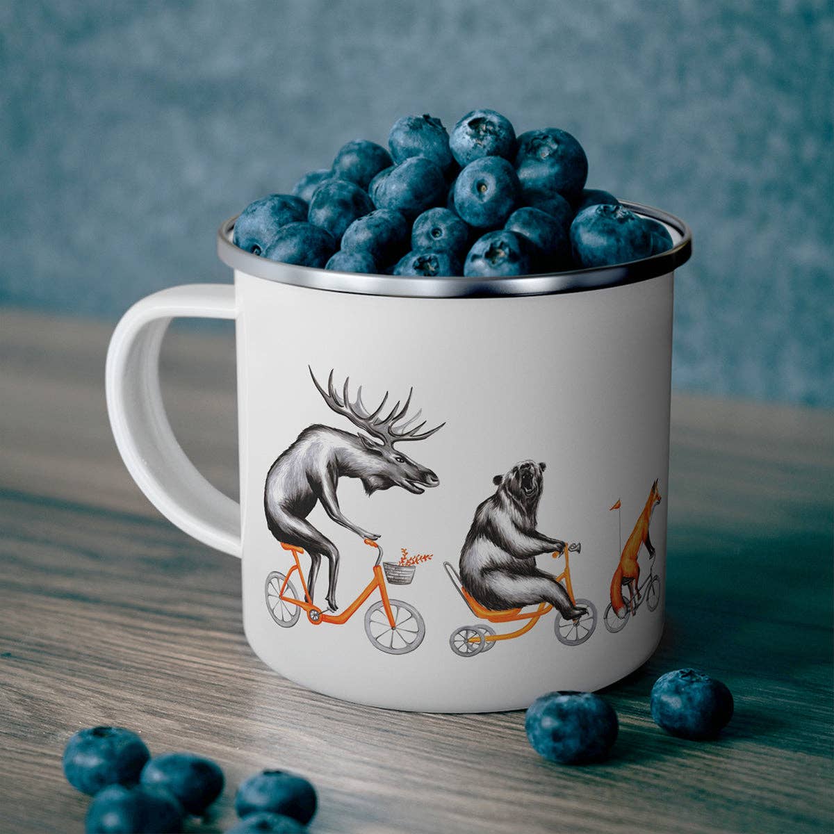 Mug with animal illustrations filled with blueberries on a wooden surface.