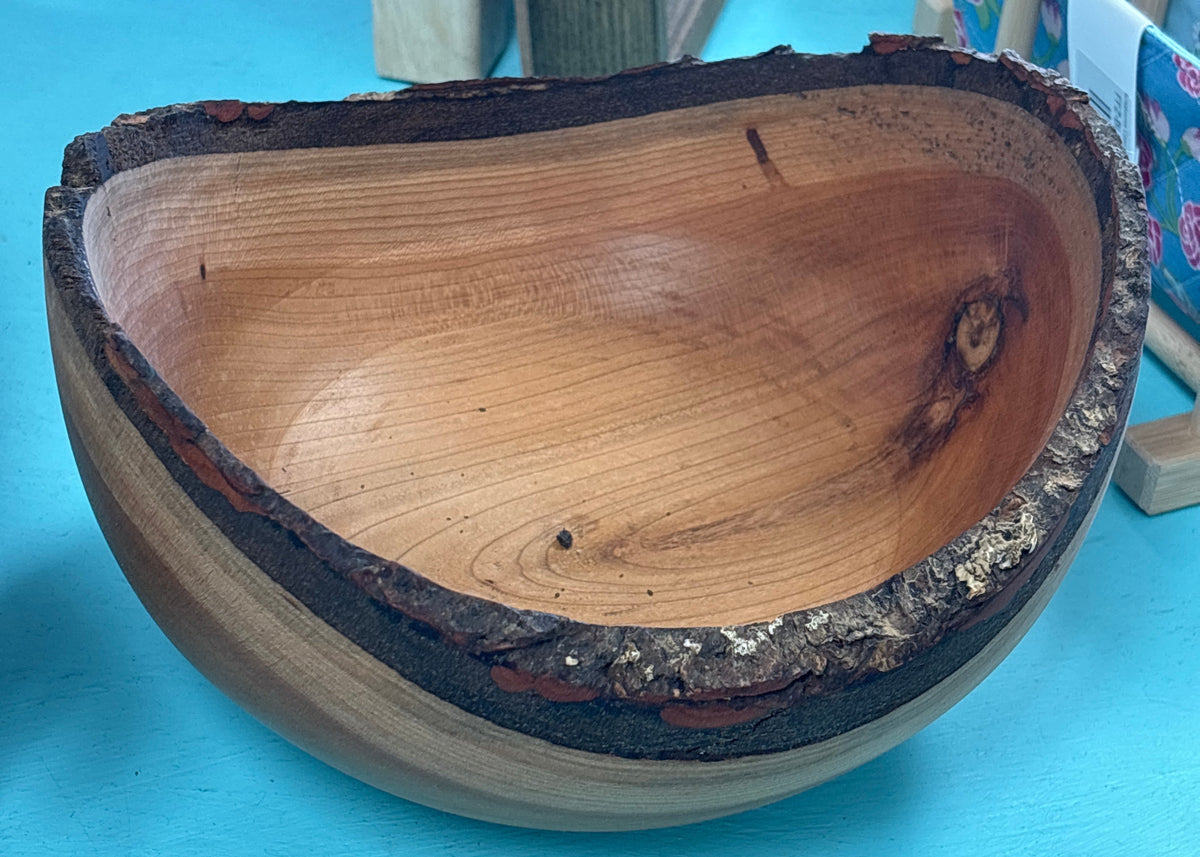 A handcrafted wooden bowl with a natural bark edge, displayed on a bright turquoise surface.