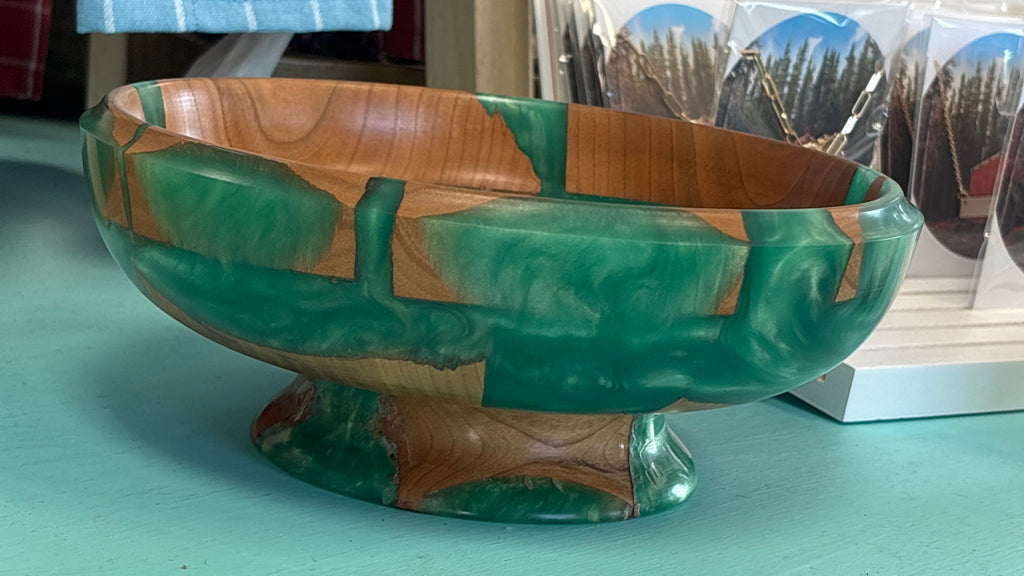 A handcrafted wooden bowl with a green and brown marbled pattern, displayed on a turquoise surface with a blue striped towel and a 'I Love Canada' card in the background.