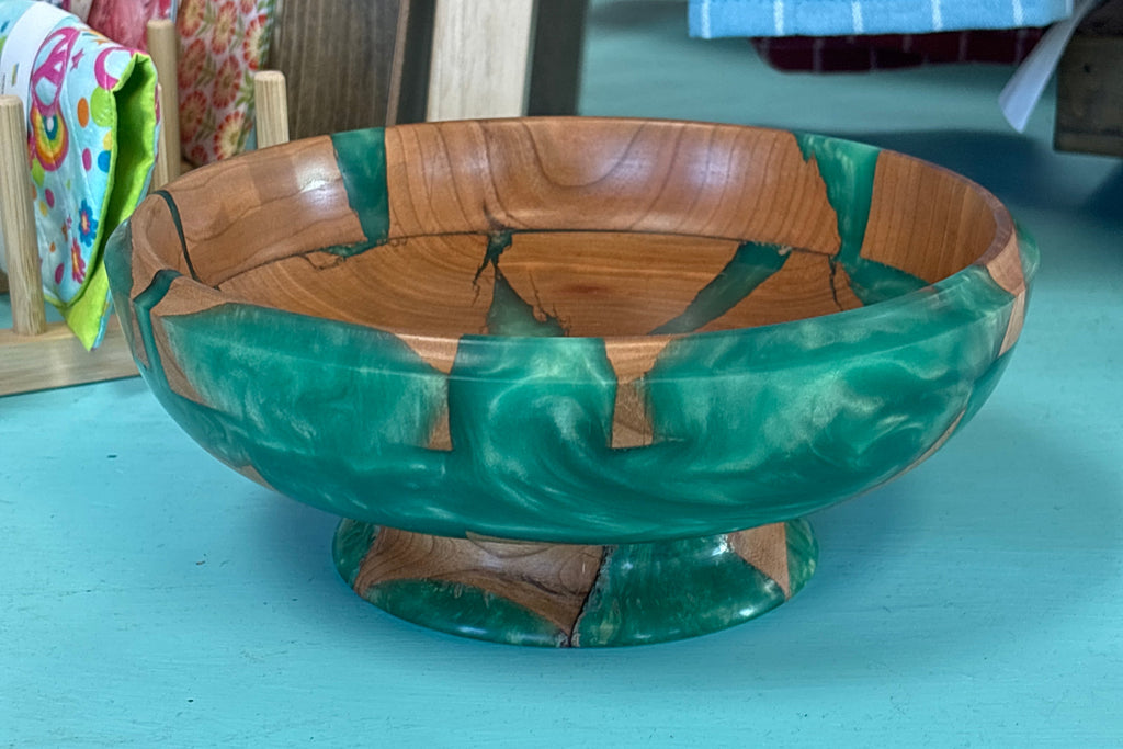 A decorative wooden bowl with a green and brown marbled pattern, sitting on a turquoise table in what appears to be a shop setting.
