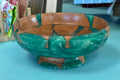 A decorative wooden bowl with a green and brown marbled pattern, sitting on a turquoise table in what appears to be a shop setting.