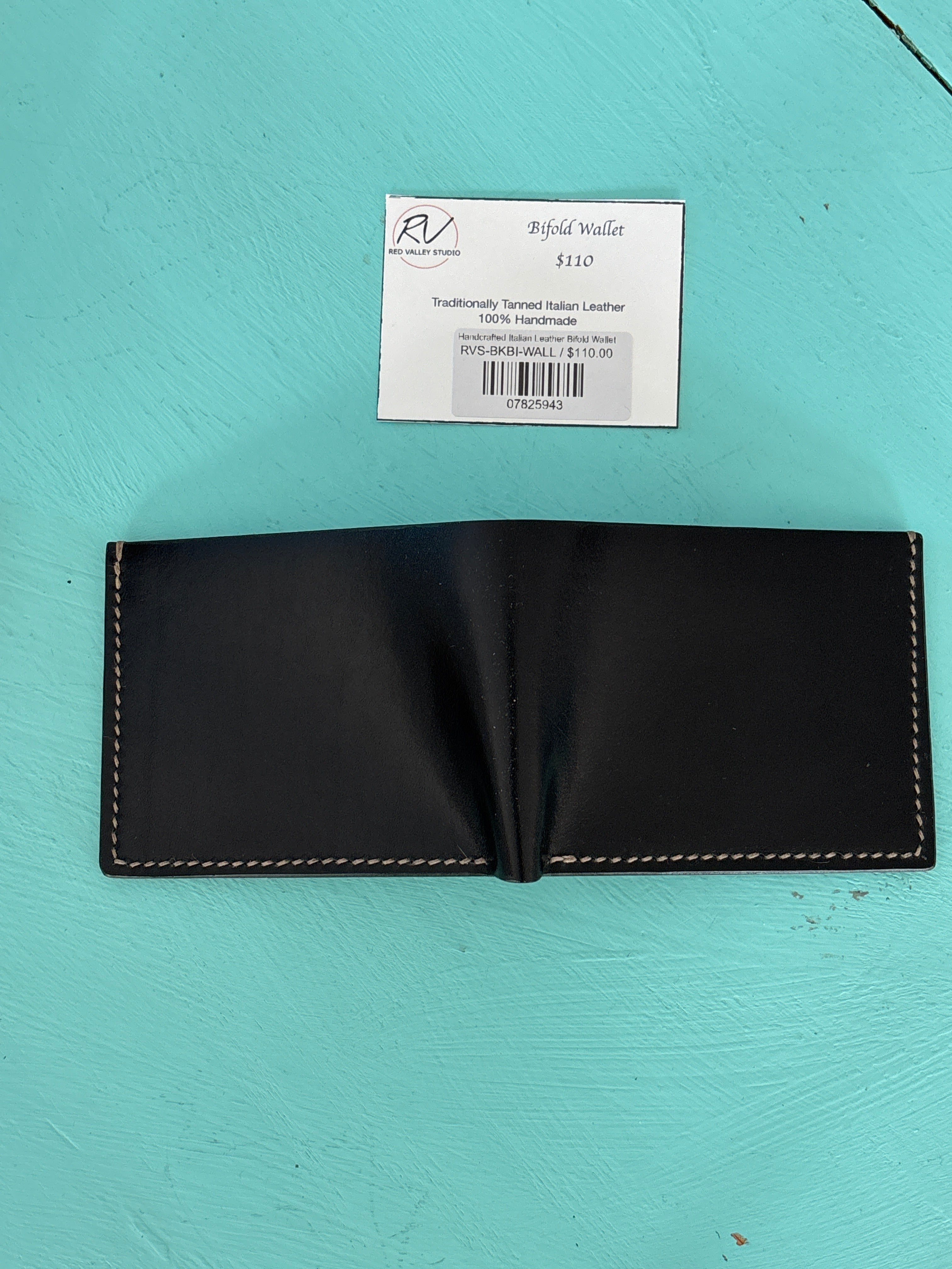 Black leather wallet on a turquoise surface with a price tag attached.