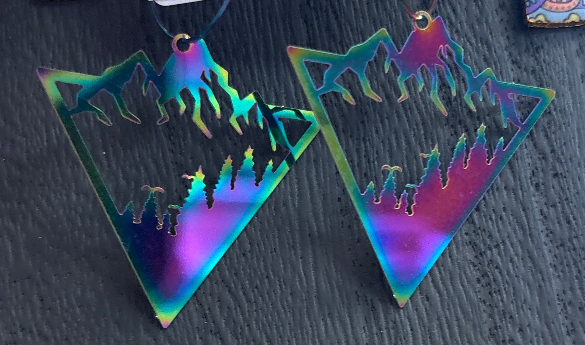 Holographic triangle-shaped earrings on a black surface with a price tag.