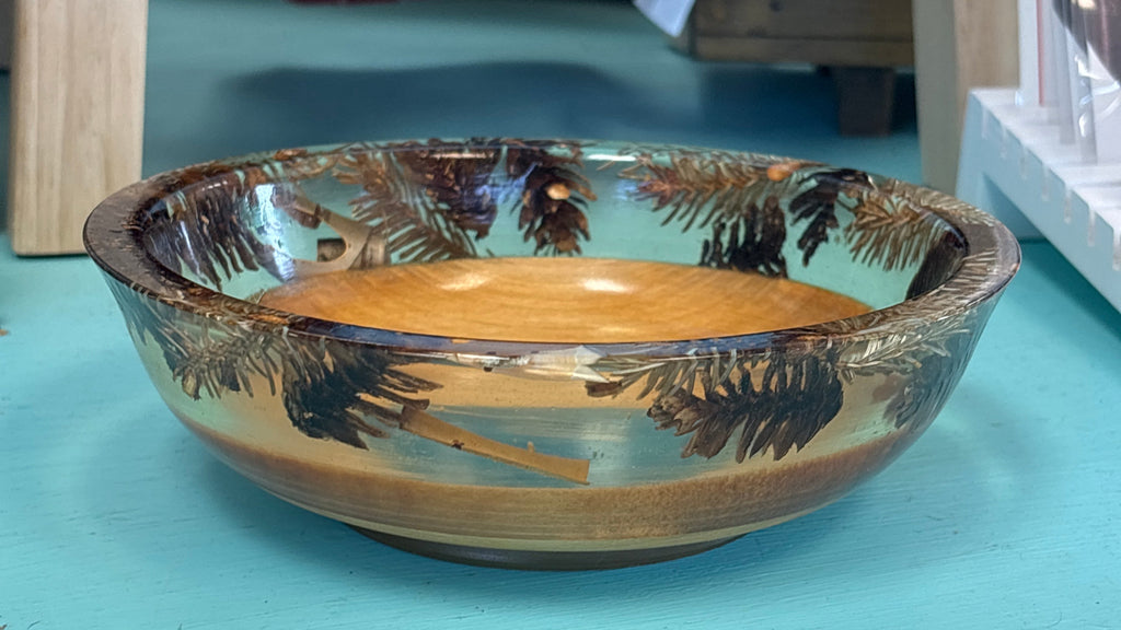 A handcrafted wooden bowl with a hand-painted tropical palm tree design, resting on a turquoise surface.