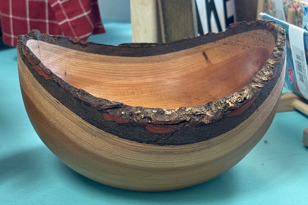 A handcrafted wooden bowl with a natural bark edge, sitting on a turquoise painted wooden table in a shop setting.