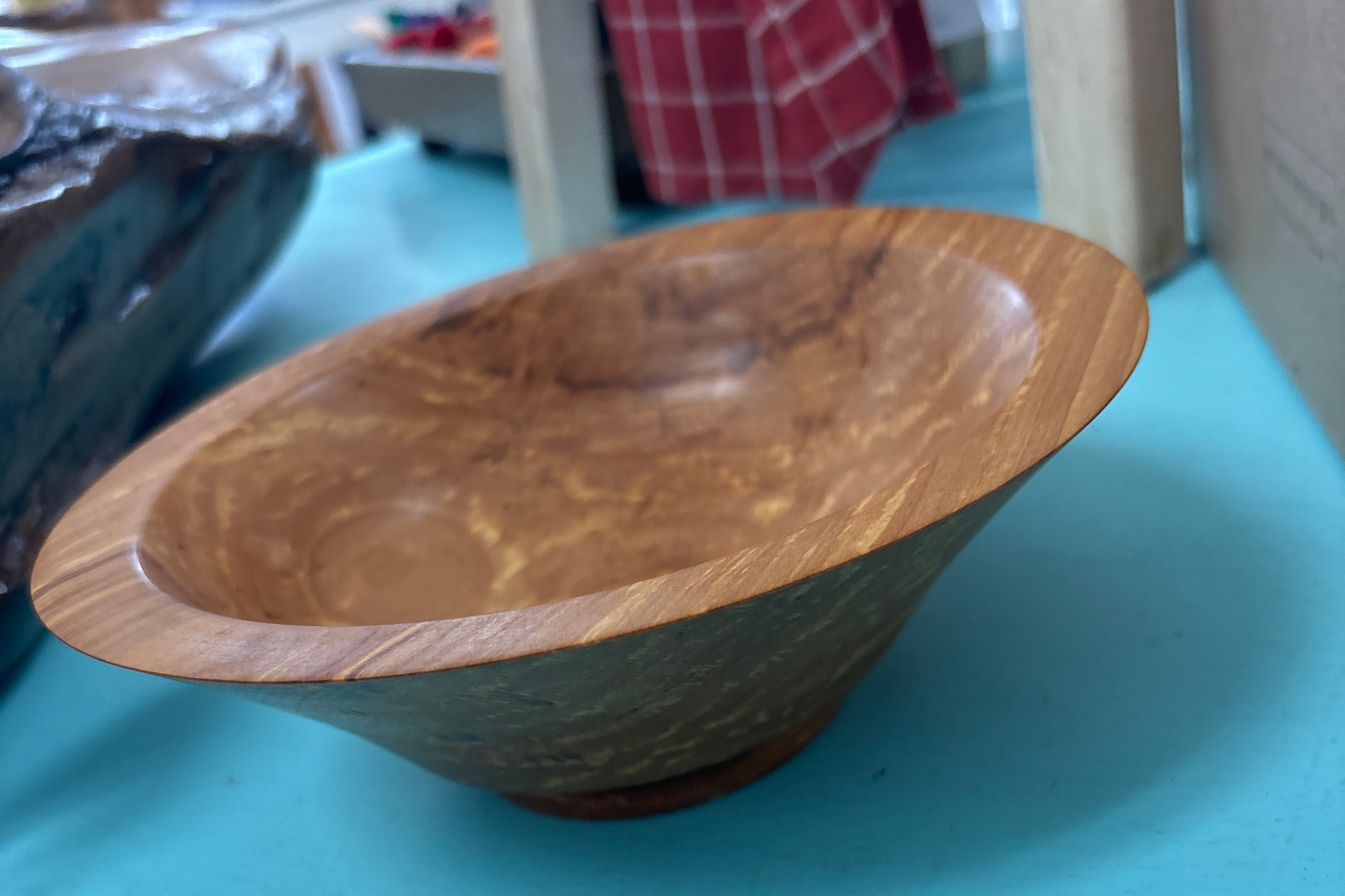 A handcrafted wooden bowl with a rich brown grain pattern, resting on a bright turquoise surface.