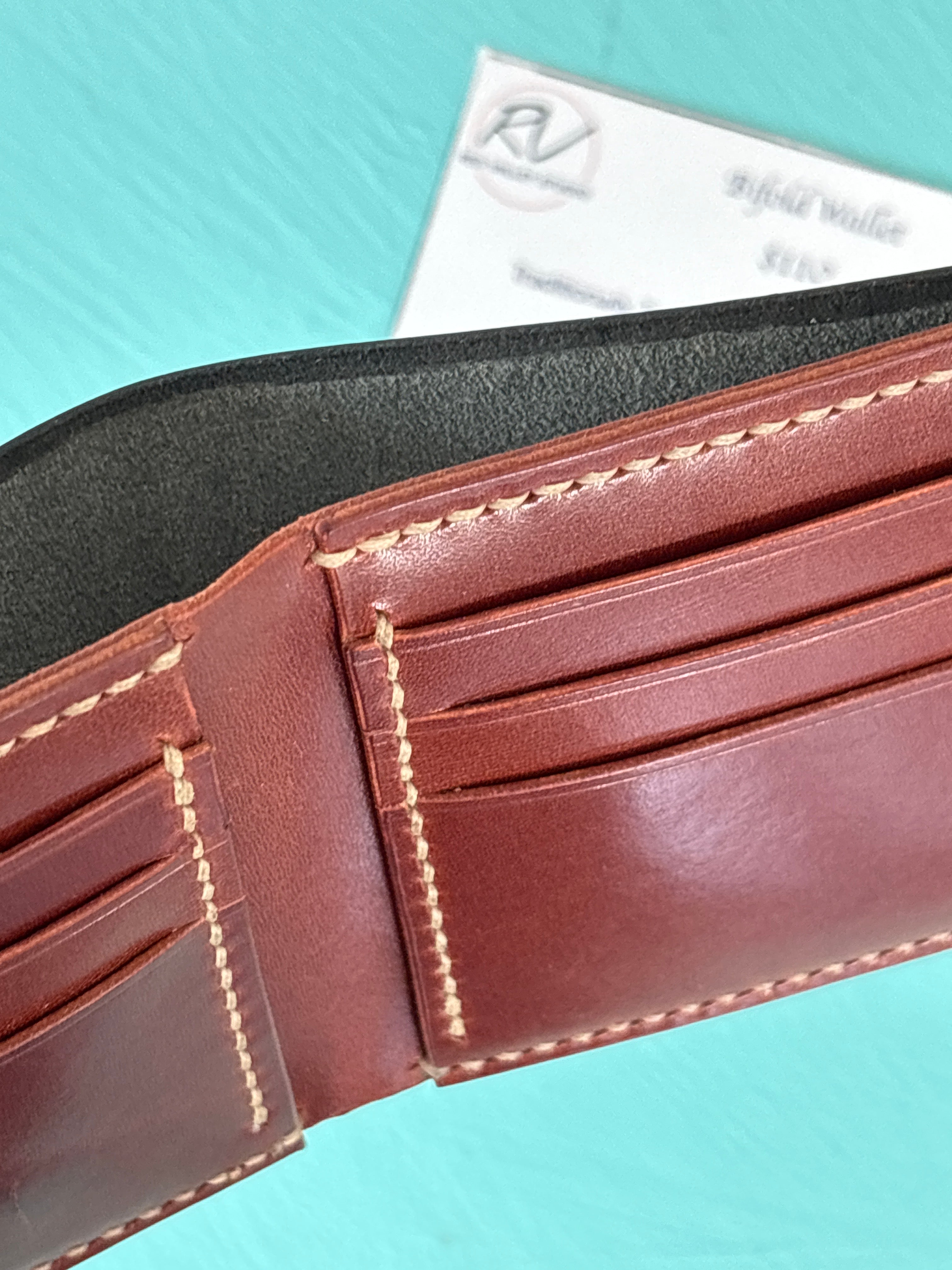 Close-up of a brown leather wallet with visible stitching on a light blue background