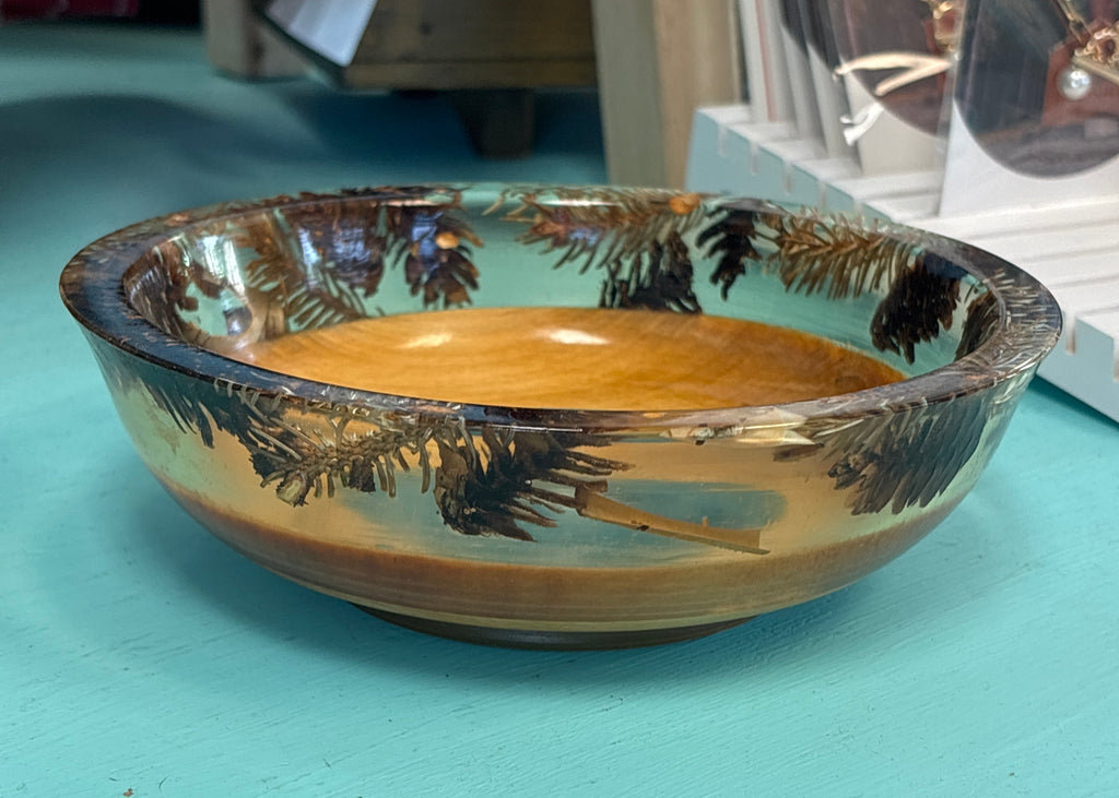 A handcrafted oval wooden bowl with a natural light brown wood center and dark brown bark-like patterns around the rim, displayed on a turquoise surface.