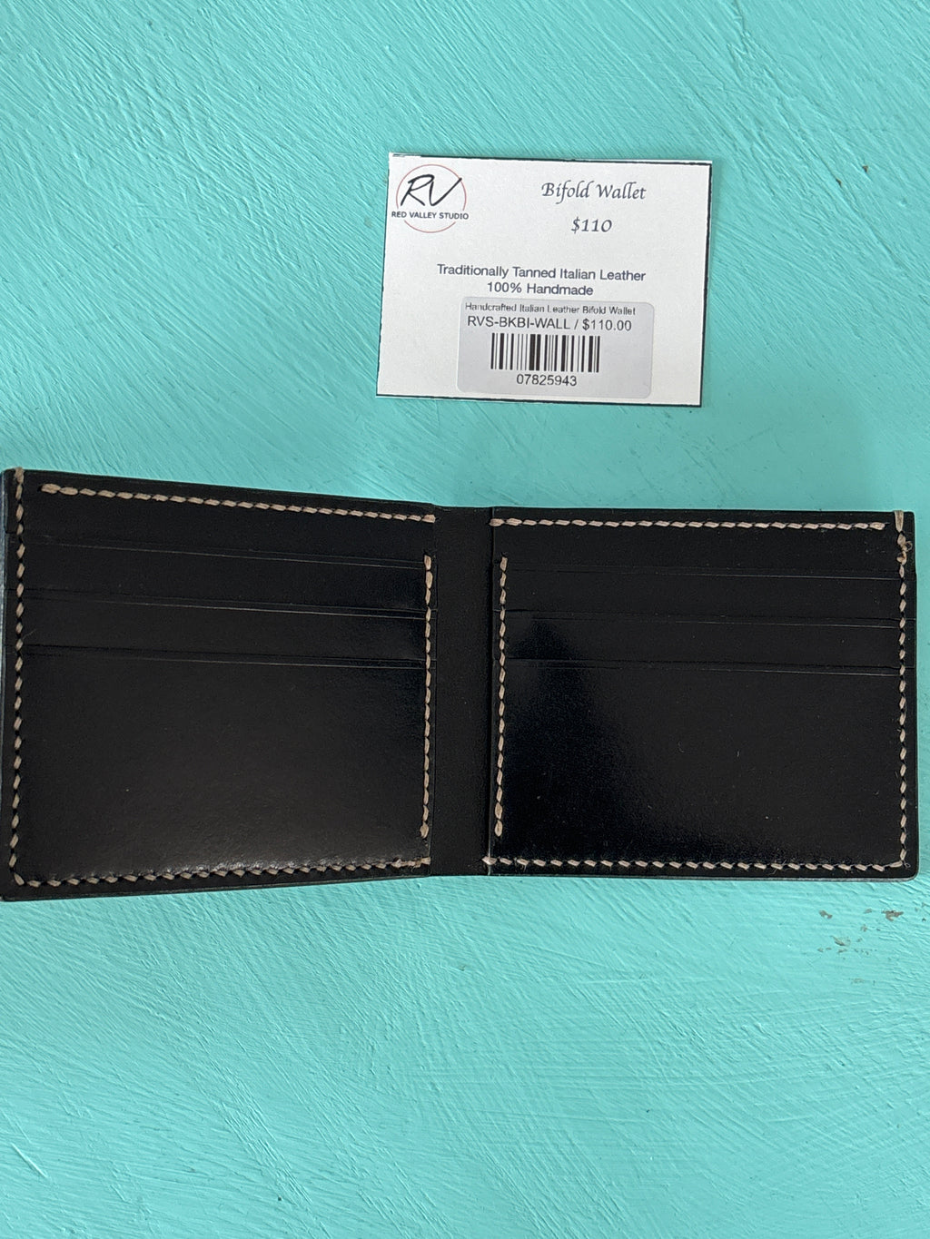 Black leather wallet with visible stitching on a turquoise background, accompanied by a label.