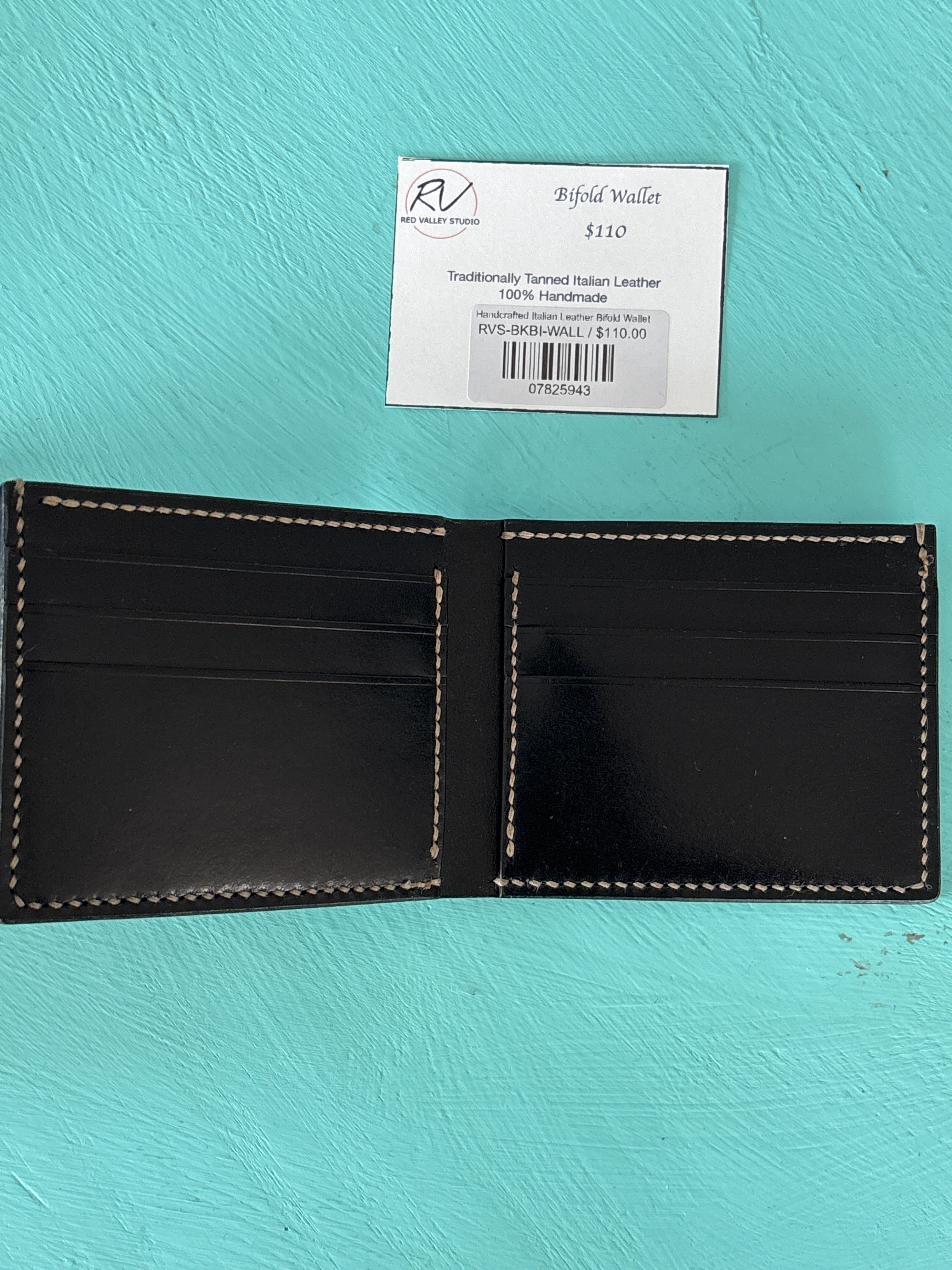 Black leather wallet with visible stitching on a turquoise background, accompanied by a label.