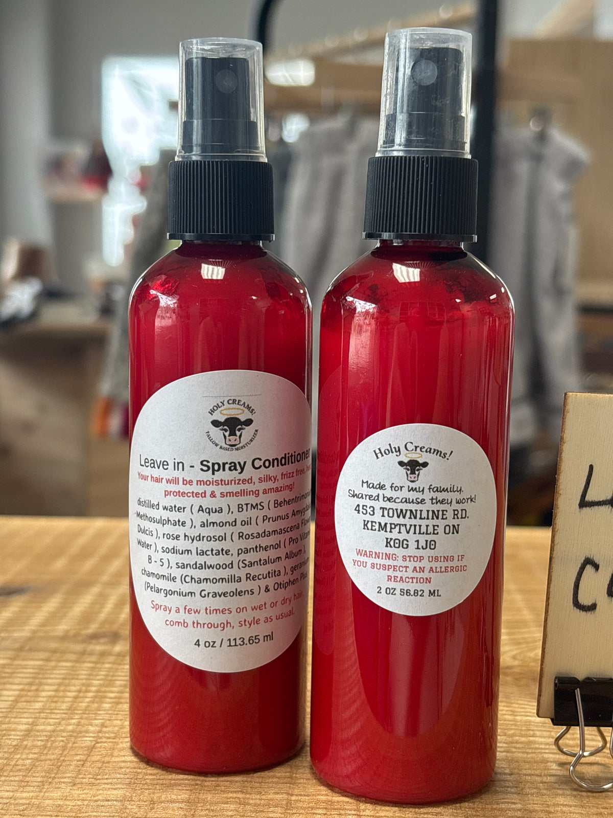 Two red spray bottles of leave in conditioner with black caps and white labels, standing on a wooden surface in a store setting.