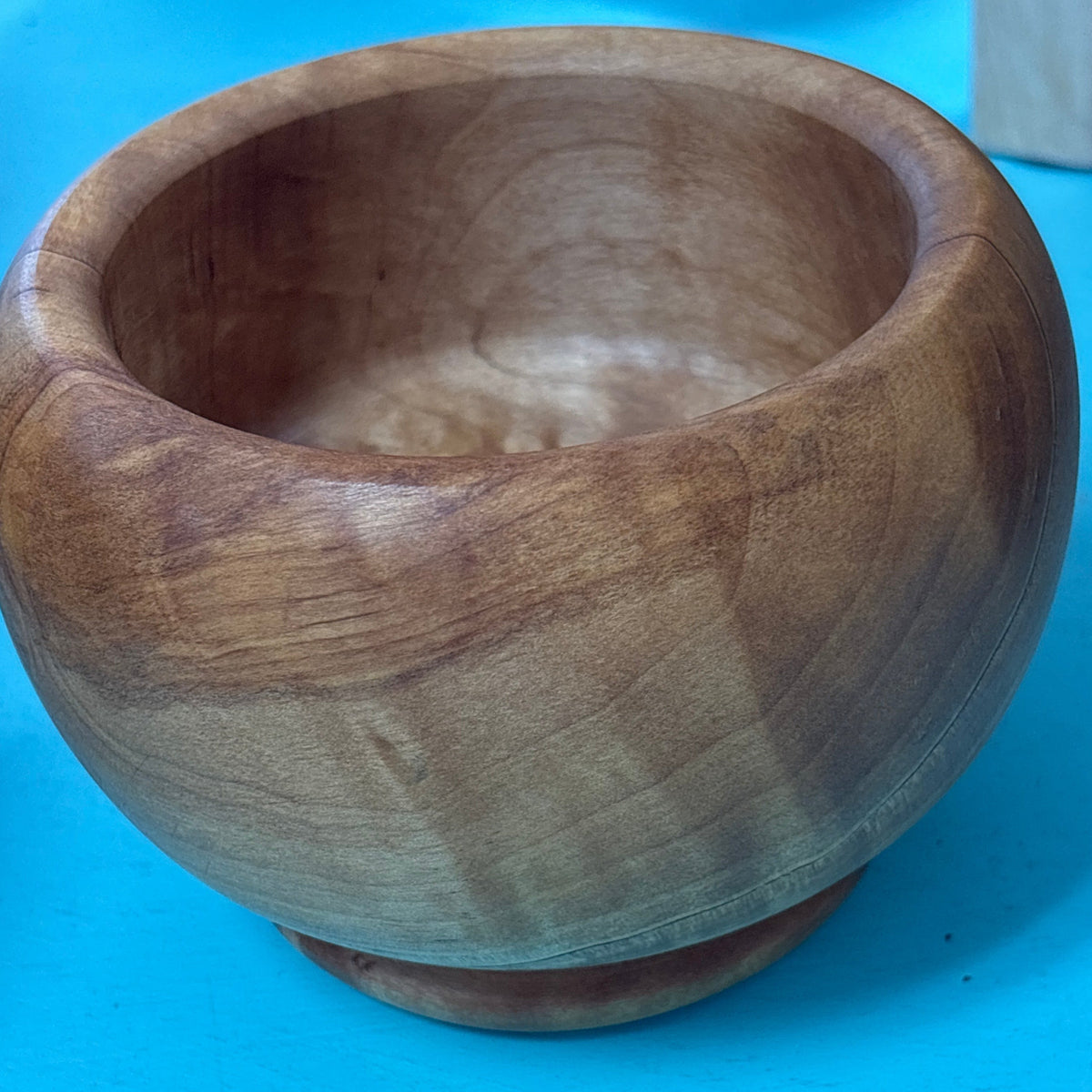 A round handcrafted wooden bowl with a thick base, showing natural wood grain, set against a bright blue background.