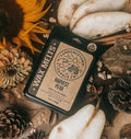 A styled flat-lay of a wax melt package labeled 'Wrenchock Farm Co. Harvest Pear' surrounded by autumn props including a sunflower, pears, pinecones, cinnamon sticks, star anise, and dried leaves on burlap.