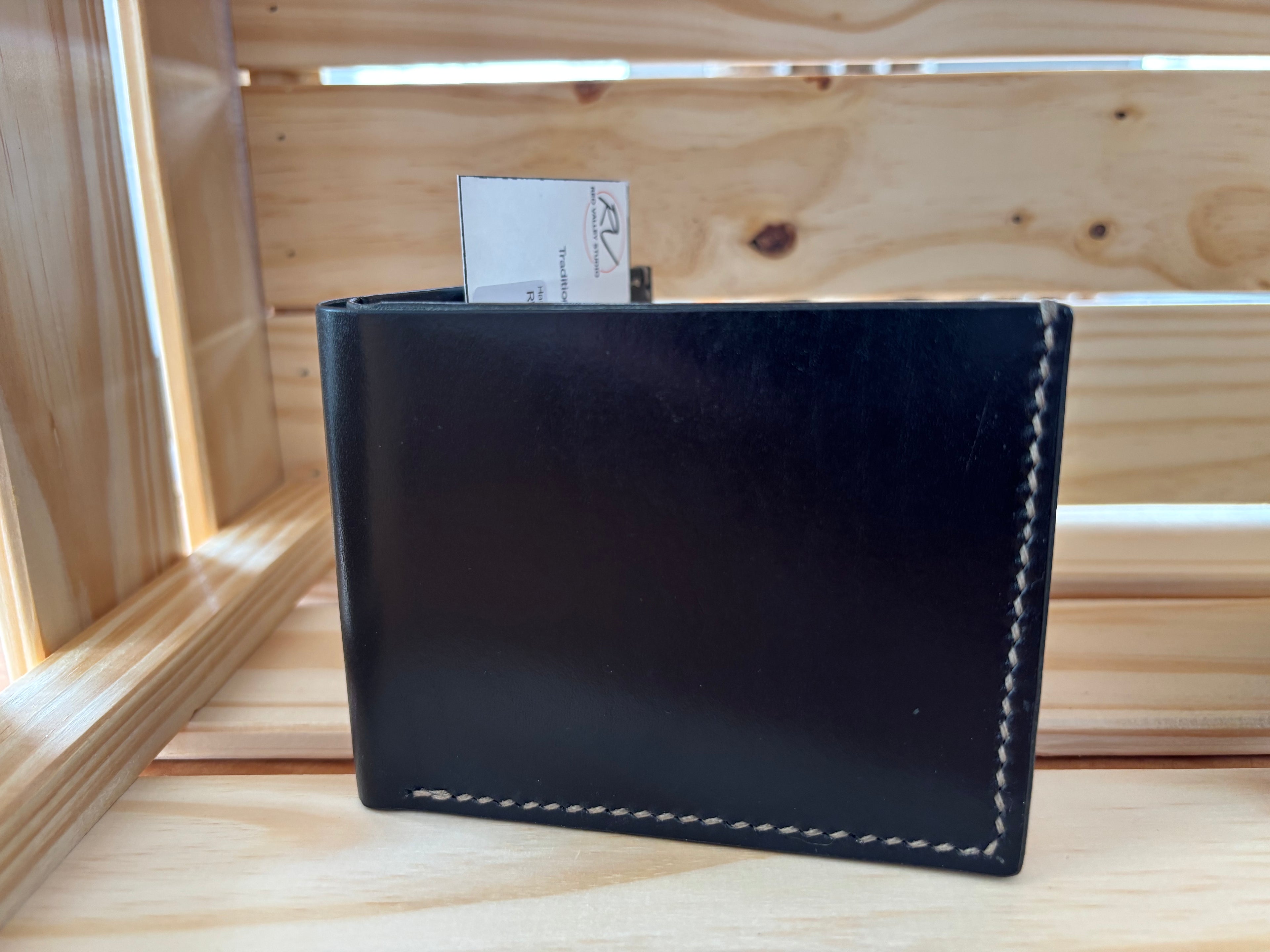 Black leather wallet with white stitching on a wooden surface
