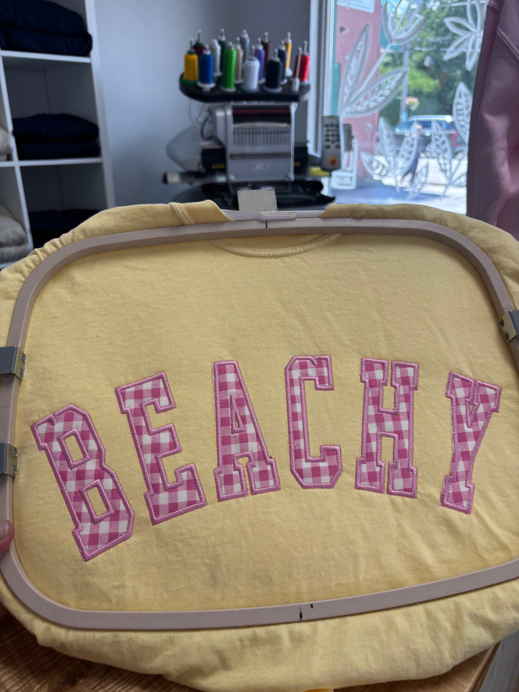 butter tshirt in embroidery hoop with 'BEACHY' in pink checkered letters in a casual setting.