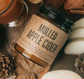 A jar of Mulled Apple Cider by The Art of Brewing Ale House & Co. styled in a rustic flat-lay with sliced apples, cinnamon sticks, star anise, dried apple slices, and pinecones.