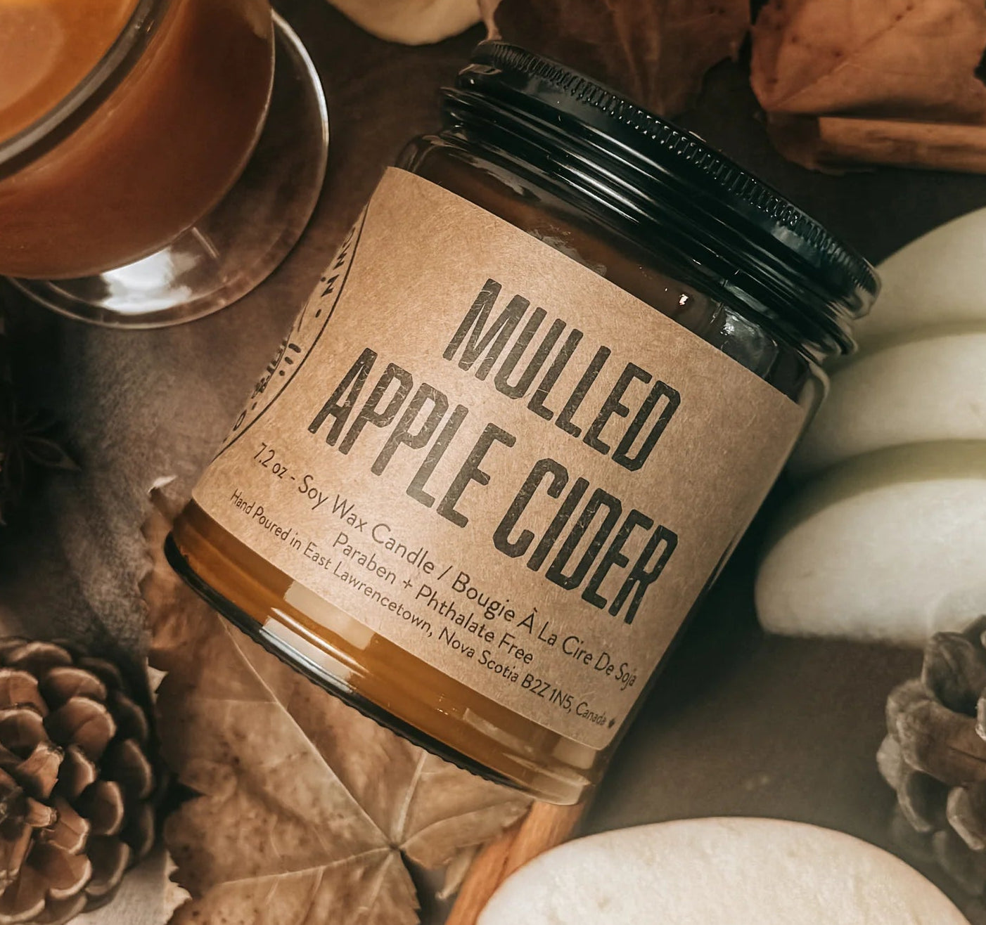 A jar of Mulled Apple Cider by The Art of Brewing Ale House & Co. styled in a rustic flat-lay with sliced apples, cinnamon sticks, star anise, dried apple slices, and pinecones.