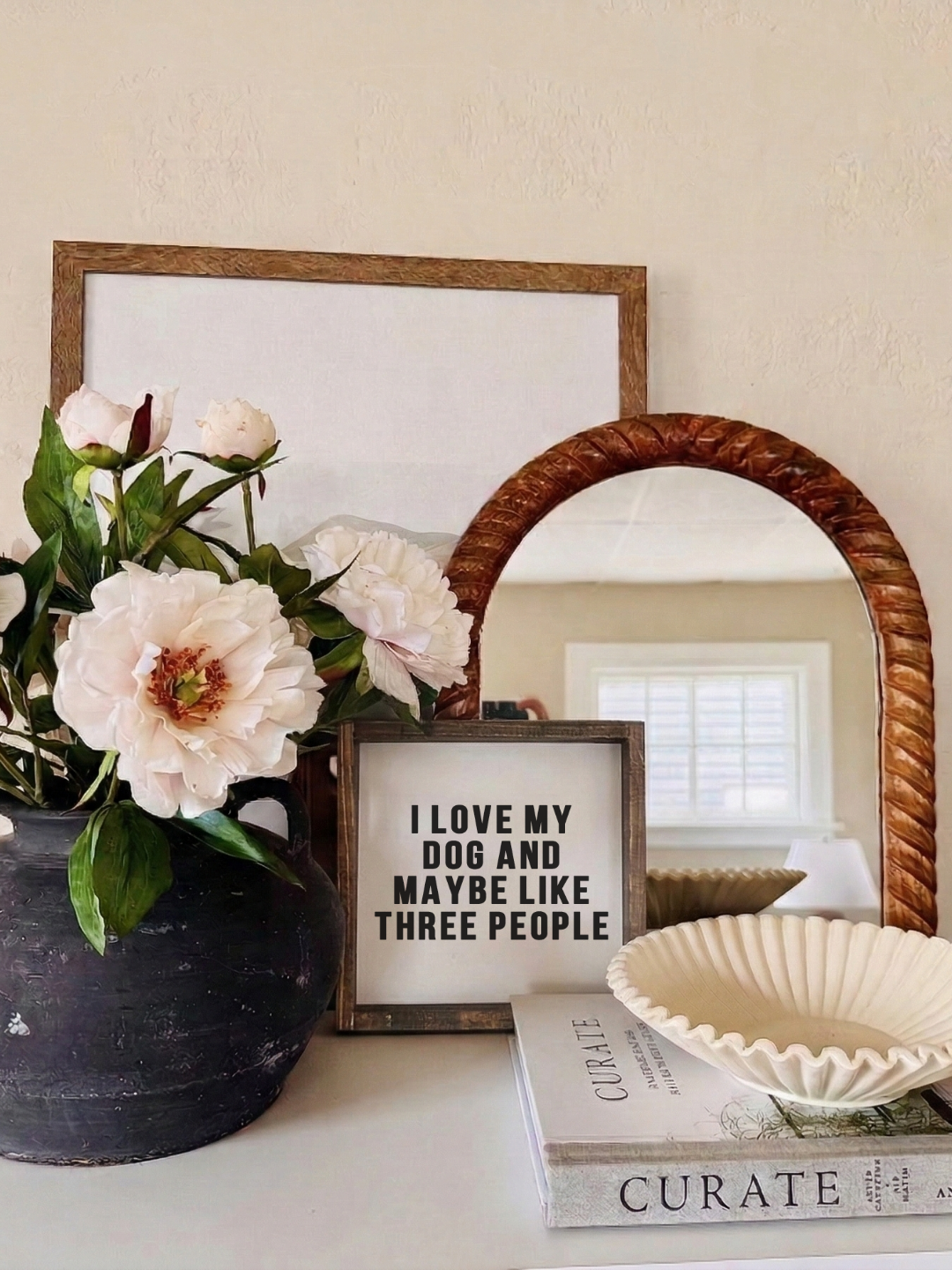 Decorative setup with flowers, framed text, mirror, and books on a surface.