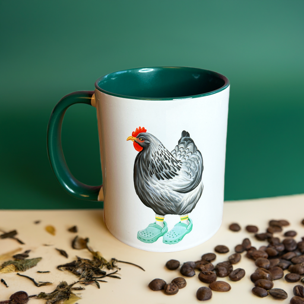 Mug with a rooster design on a surface with coffee beans and tea leaves.