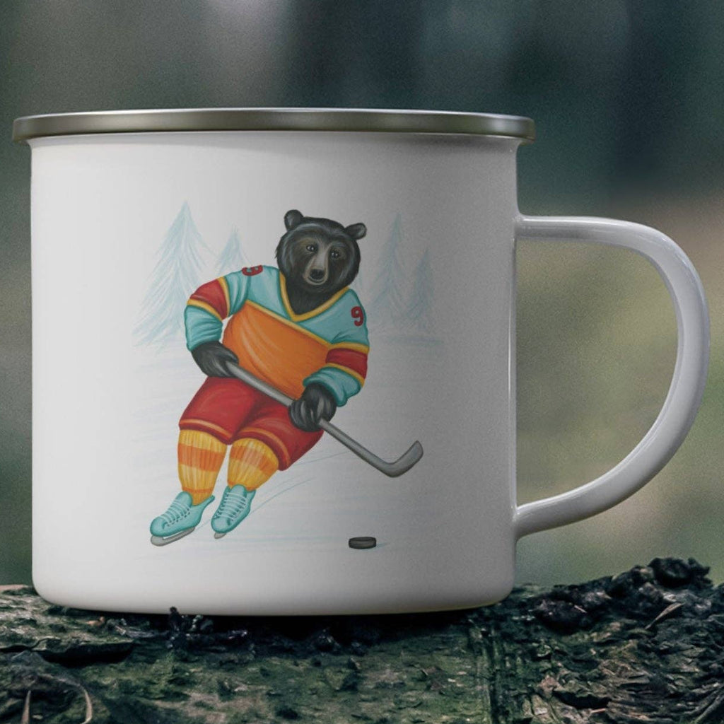 White mug with a bear playing hockey design on a wooden log in a forest setting