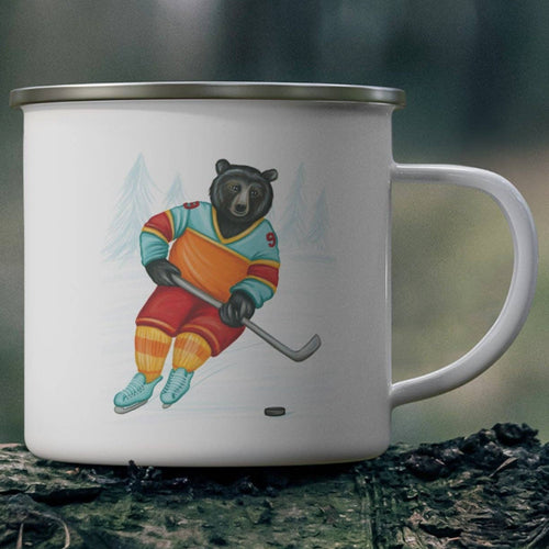 White mug with a bear playing hockey design on a wooden log in a forest setting