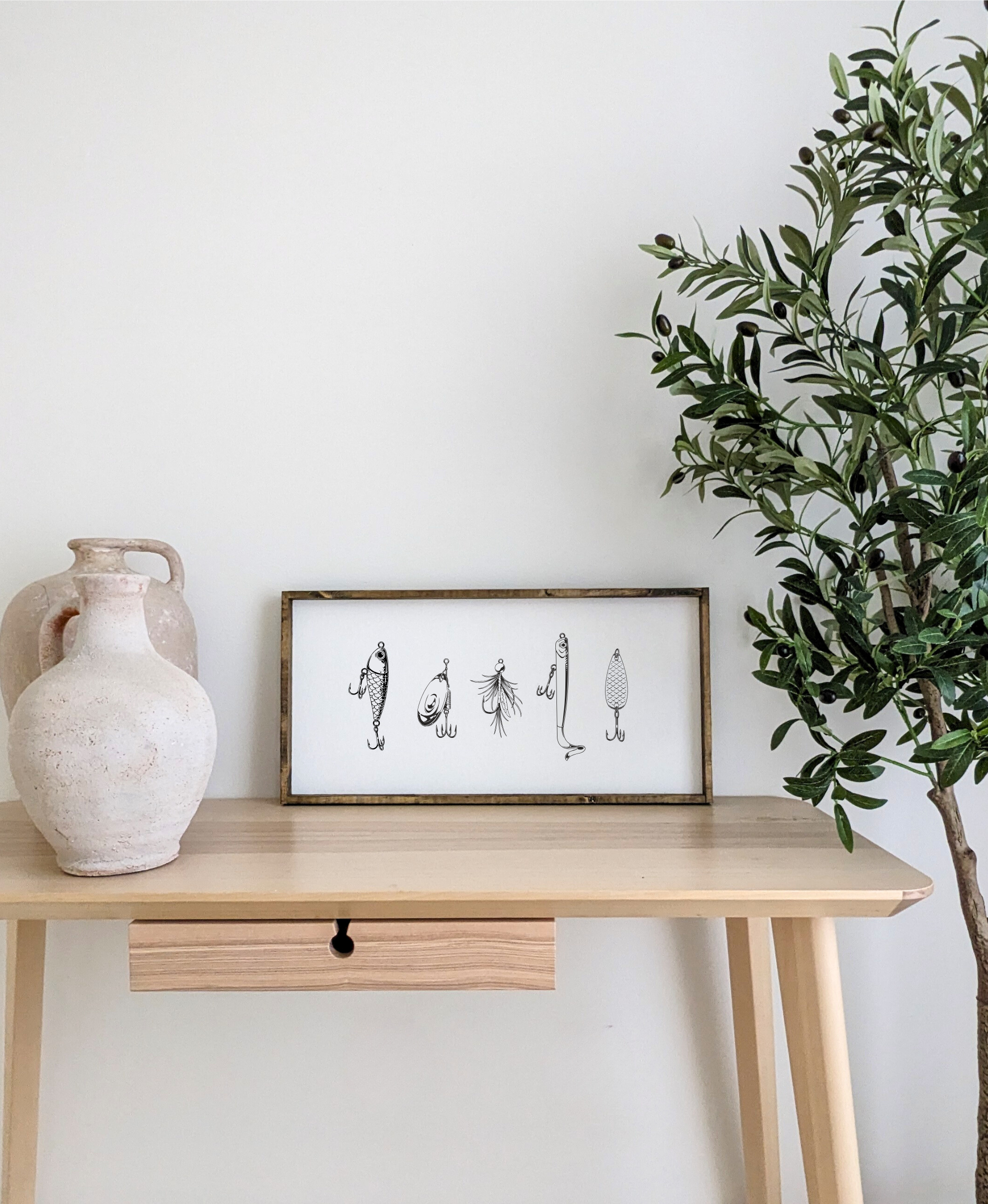 Wooden desk with a framed artwork and a vase, against a white wall with a plant on the right.
