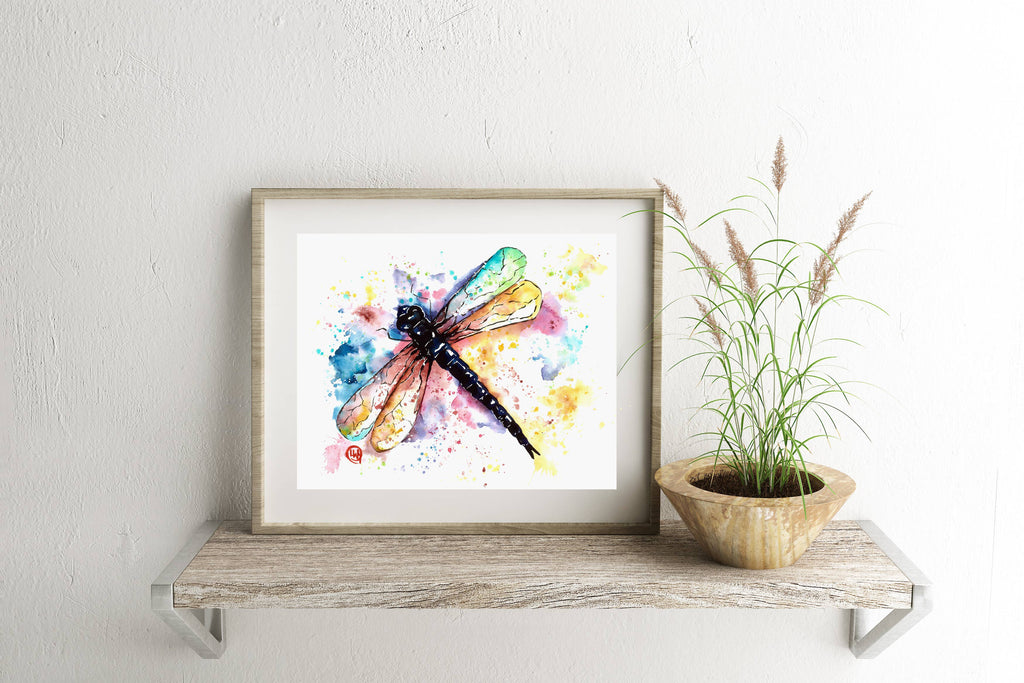 Framed artwork of a colorful dragonfly on a wooden shelf with a plant.